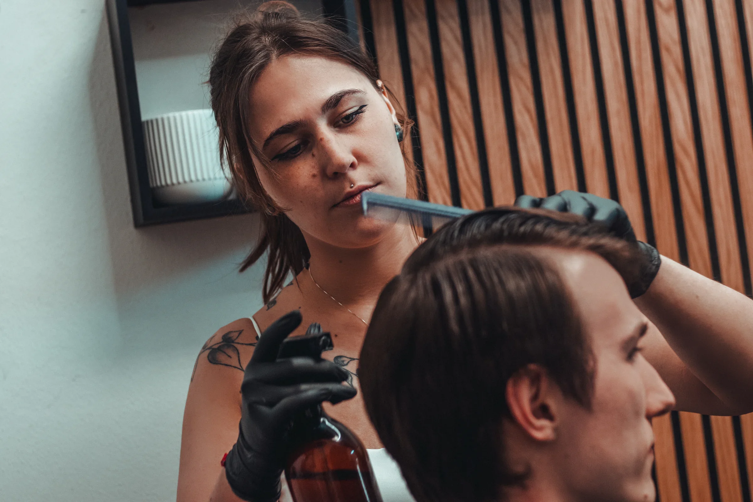 Barberka v Medusa Barber v Plzni češe zákazníkovi vlasy hřebenem a v druhé ruce drží sprej na styling